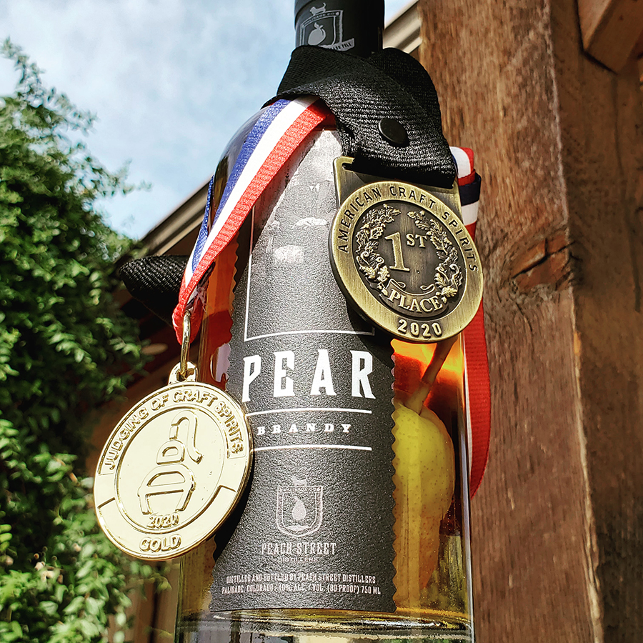 A bottle of pear brandy hangs outside, adorned with two gold medals—perfect for a late night bar and grill or anyone seeking craft cocktails made from an award-winning distillery.