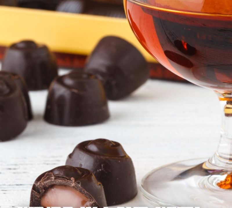 A close-up of assorted chocolate truffles beside a glass of amber-colored spirit, with a box of chocolates in the background. White text reads, We’re in love with pairing chocolate and spirits. Peach Street Distillers logo is at the top.