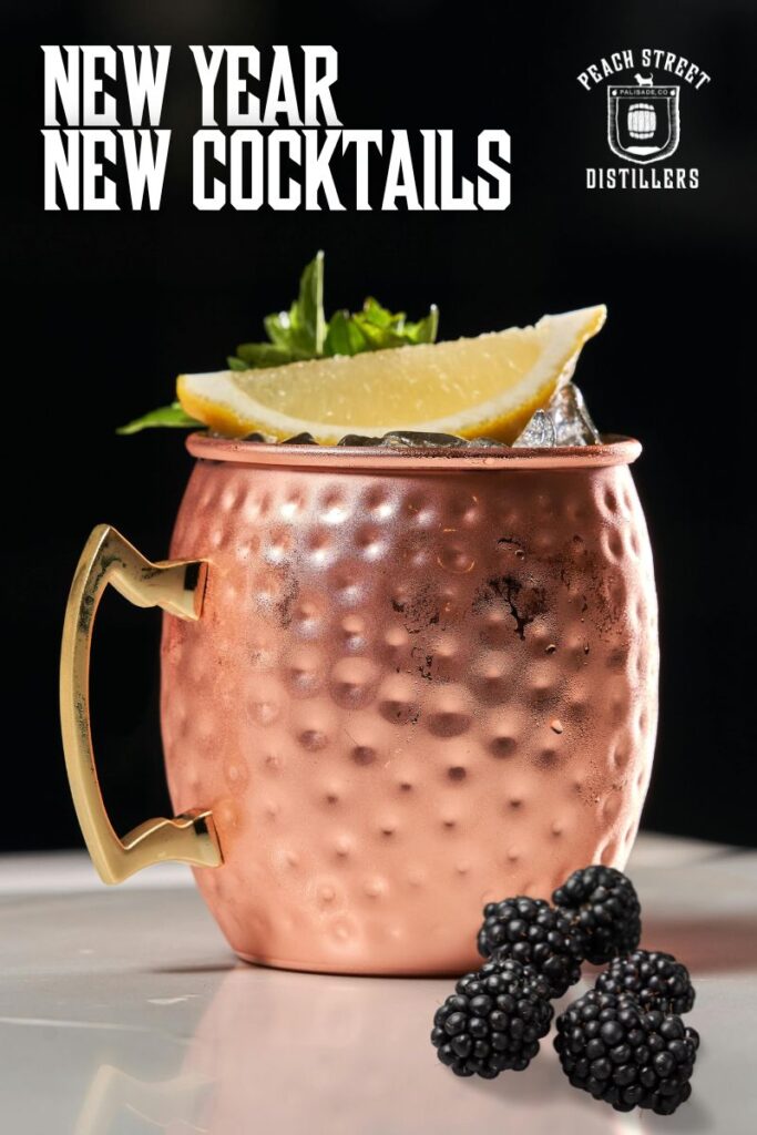 A copper mug filled with a cocktail, garnished with a lemon wedge, mint, and blackberries, sits on a white surface. Text reads New Year New Cocktails and Peach Street Distillers—featuring New Cocktails for January.