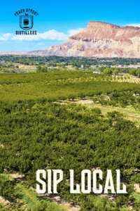 A panoramic view of a lush green orchard in Palisade, Colorado, with a mesa in the background under a blue sky. Text reads PEACH STREET DISTILLERS at the top and SIP LOCAL at the bottom—perfect for celebrating Earth Month.