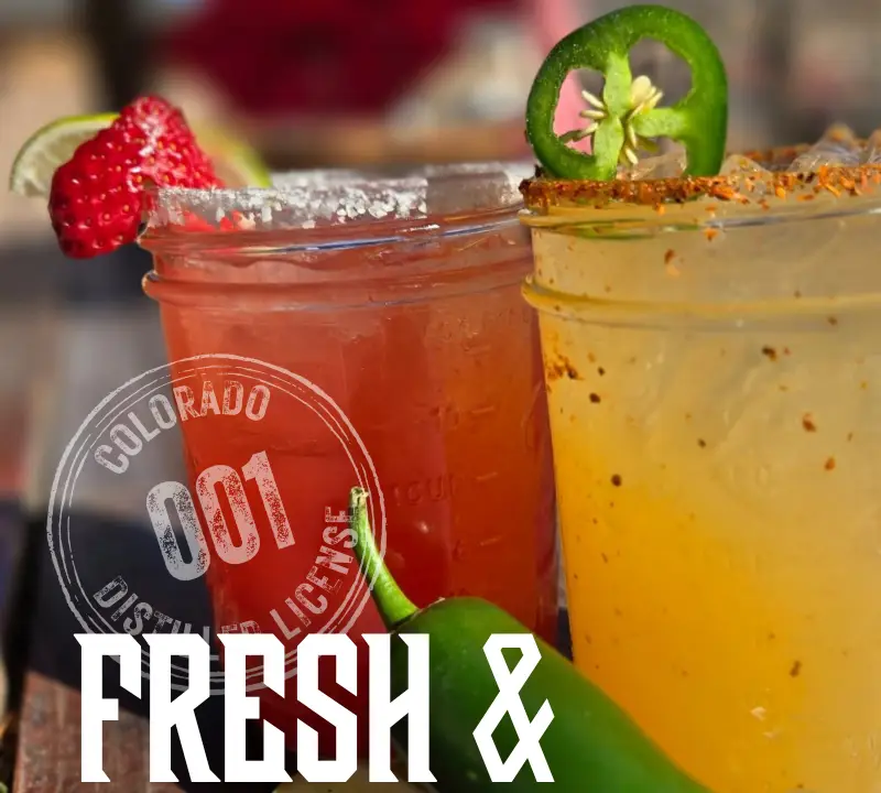 Two colorful cocktails in mason jars, one red with a strawberry garnish and one yellow with a jalapeño garnish, sit on a sunny outdoor table; text reads “Fresh & Local - Peach Street Distillers.