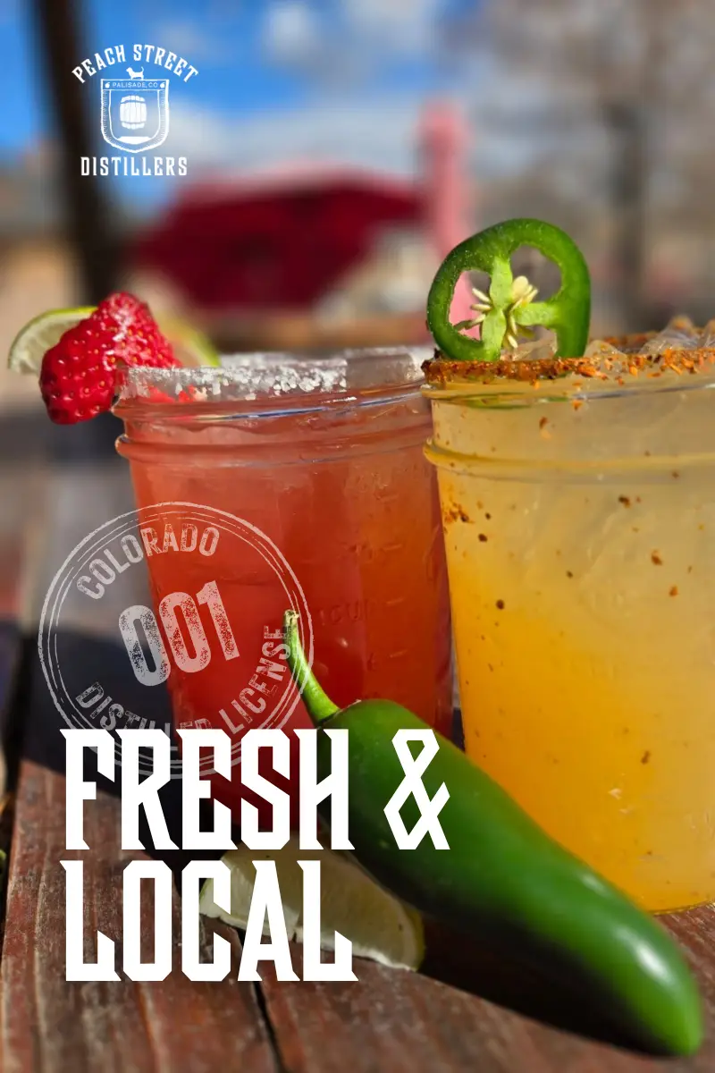 Two colorful cocktails in mason jars, one red with a strawberry garnish and one yellow with a jalapeño garnish, sit on a sunny outdoor table; text reads “Fresh & Local - Peach Street Distillers.